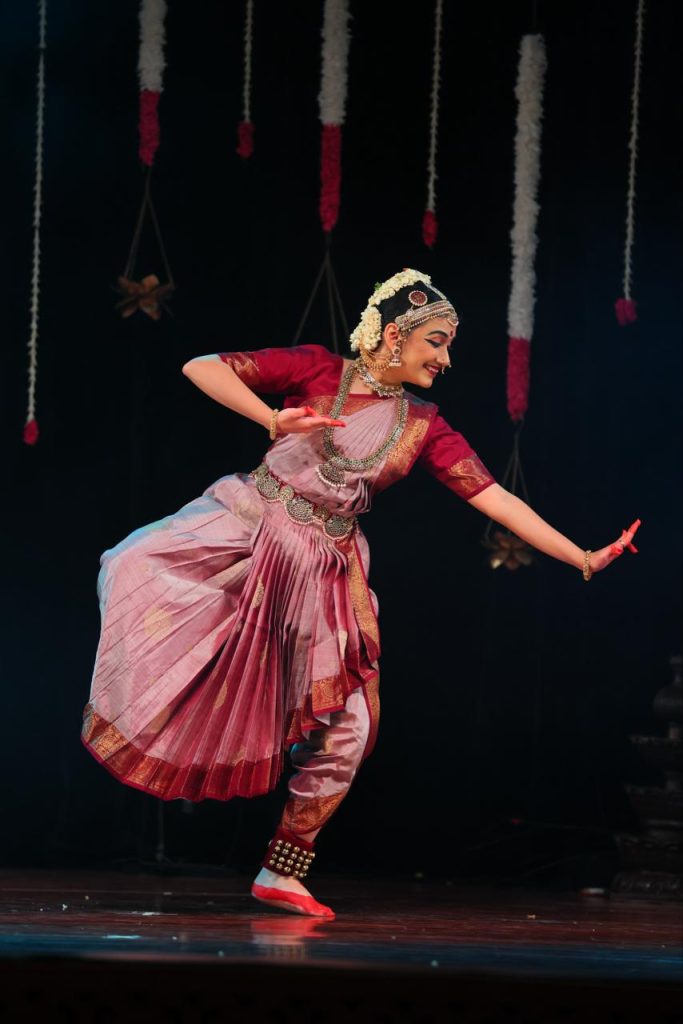 Ananya performing in a pink costume with an extended arm
